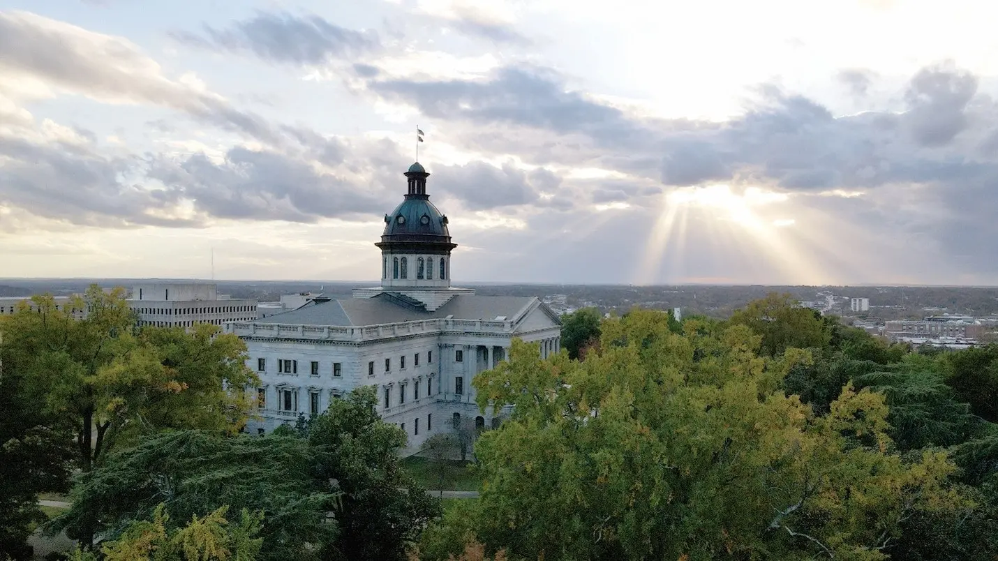  Sunlight breaking through clouds over the South Carolina State House, representing government action related to Inflation Reduction Act energy incentives that are expiring December 31, 2025. 